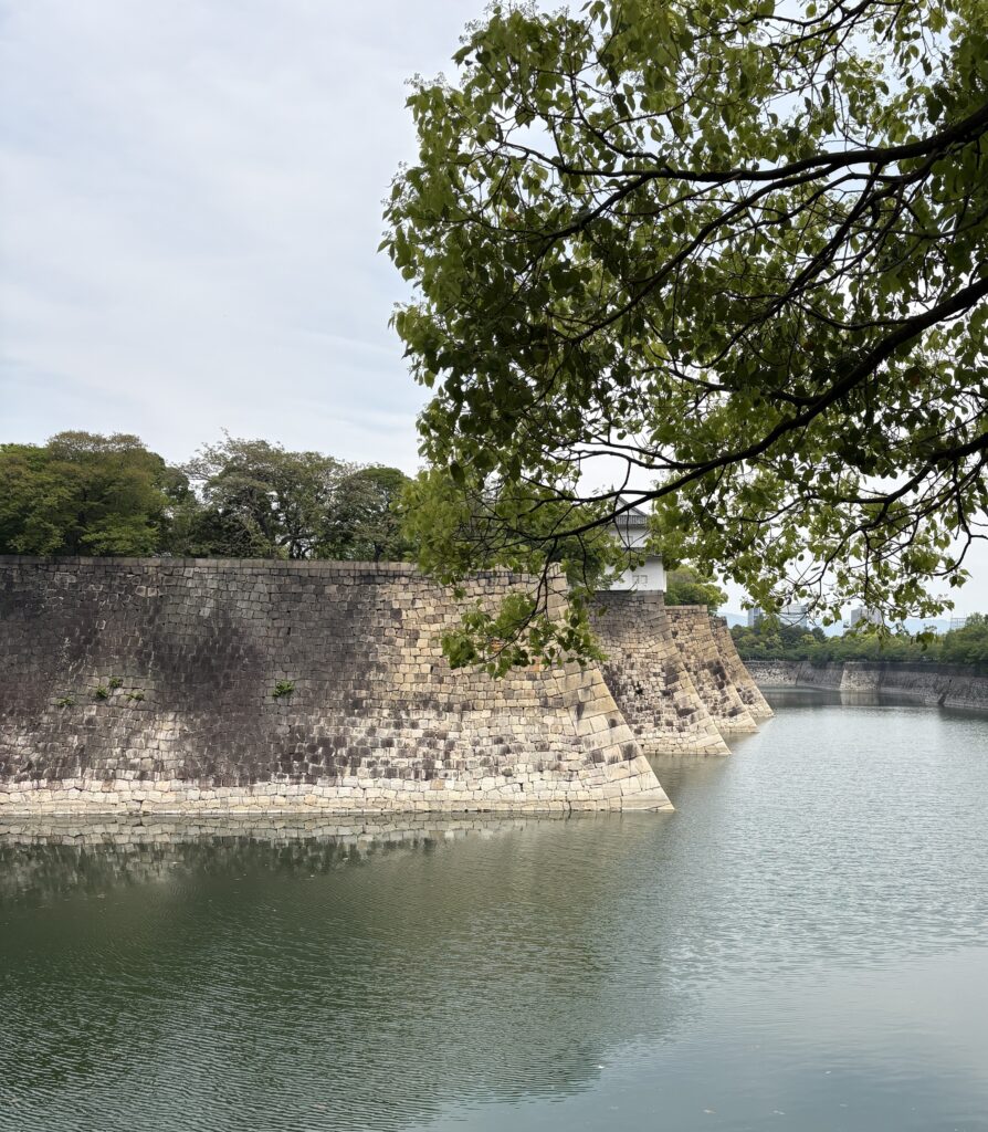 A scenic view of the wide moat surrounding Osaka Castle, reflecting the historic stone walls and greenery.