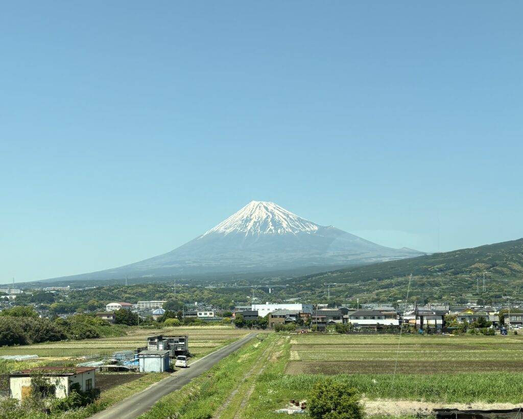 Snow-capped Mount Fuji seen from the train, framed by clear skies and passing scenery”