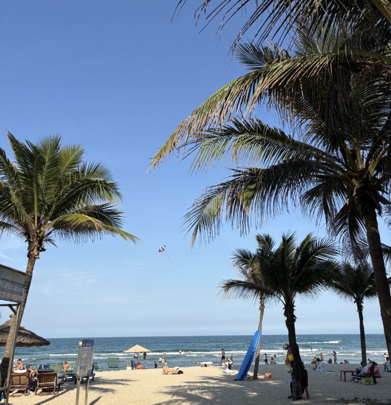 View of My Khe Beach in Da Nang on a sunny day with palm trees, clear skies, and people enjoying the beach
