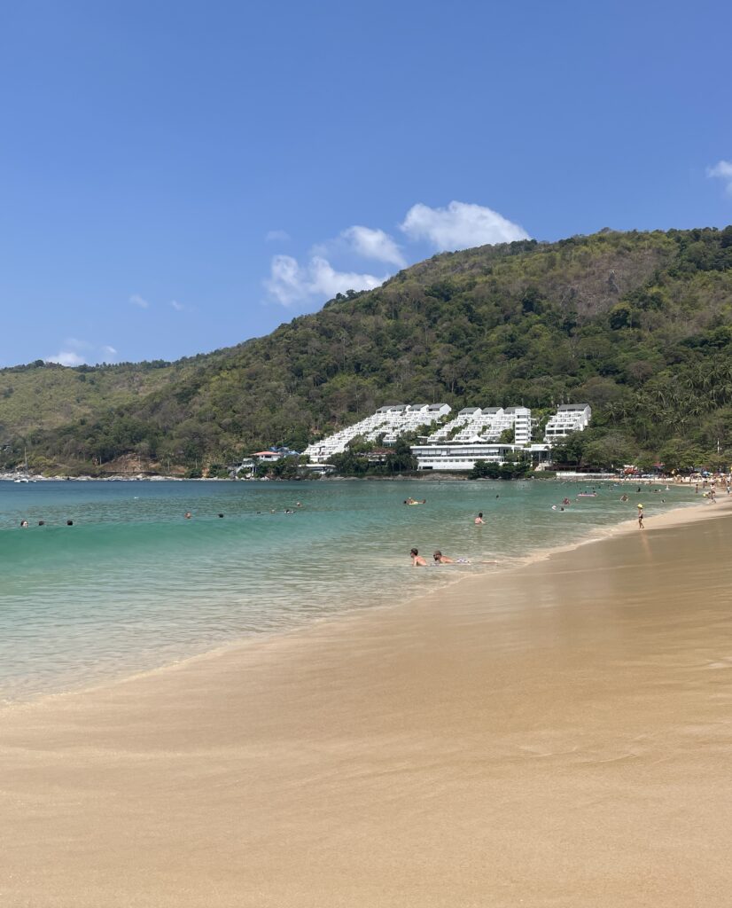 Clear turquoise water and soft sand at a quiet, nearly empty Nai Harn Beach in Phuket, Thailand
