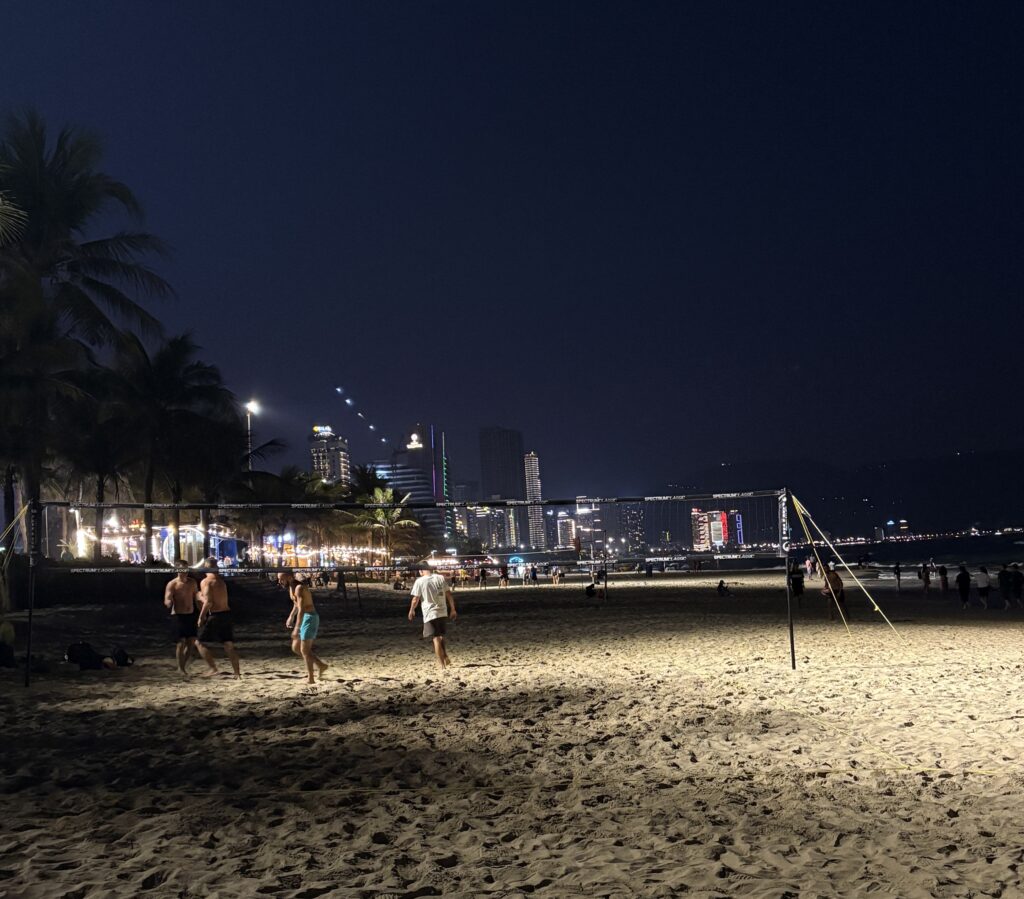 Tourists men playing volleyball under lights on My Khe Beach at night in Da Nang, Vietnam.