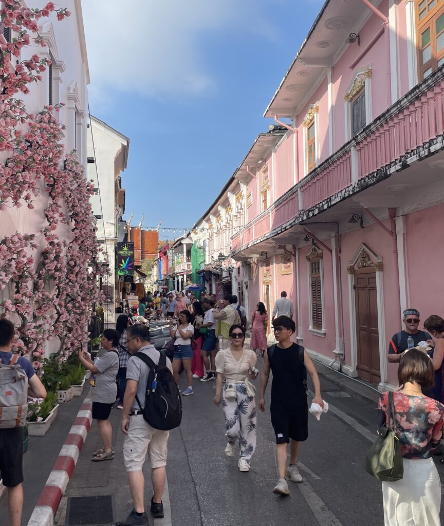 Tourists walking past pink Sino-Portuguese buildings in Old Phuket Town, Thailand
