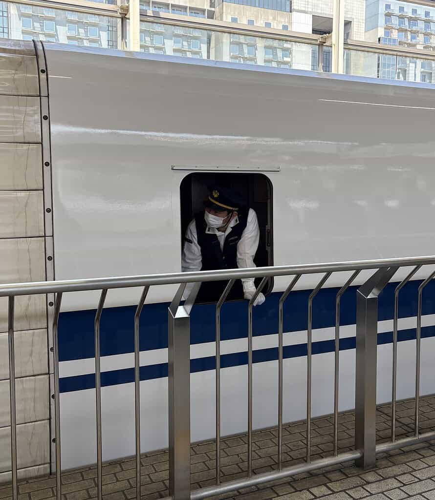 View from a bullet train window in Osaka with a uniformed train worker visible in the foreground
