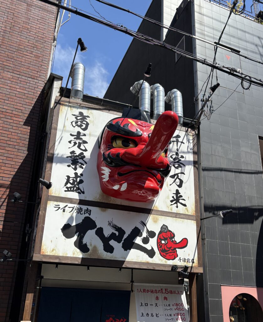 A Japanese restaurant in Osaka featuring a massive red Tengu statue with a long nose, surrounded by bold signage and lights.