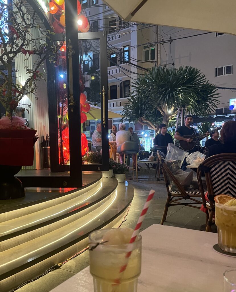 Cocktails served at PĀMA Bistro in Da Nang with a man playing guitar during a live music session, creating a cozy, laid-back evening vibe.