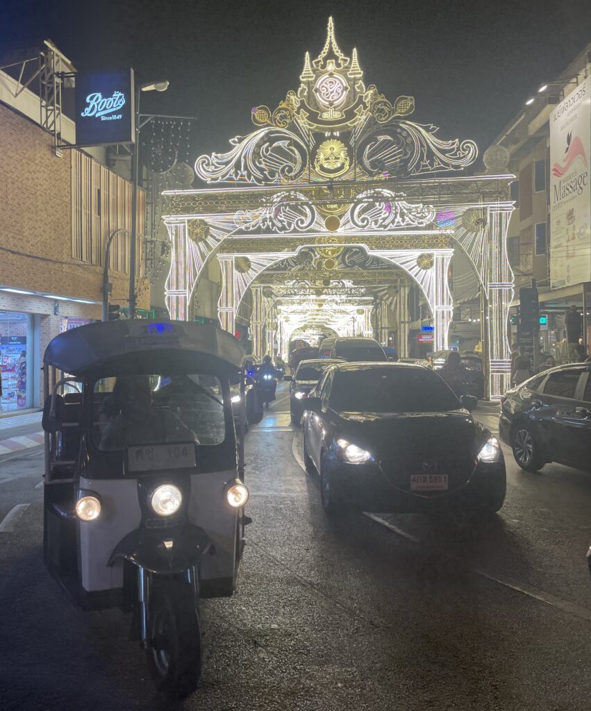 Nighttime tuk-tuk and taxi passing the illuminated arch at Tha Phae Gate outside Chiang Mai’s Old City.
