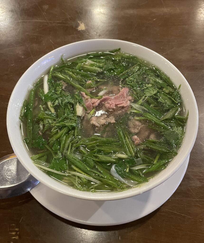 A hot bowl of pho served on a table in Hanoi just before being eaten, showcasing fresh herbs and clear broth.
