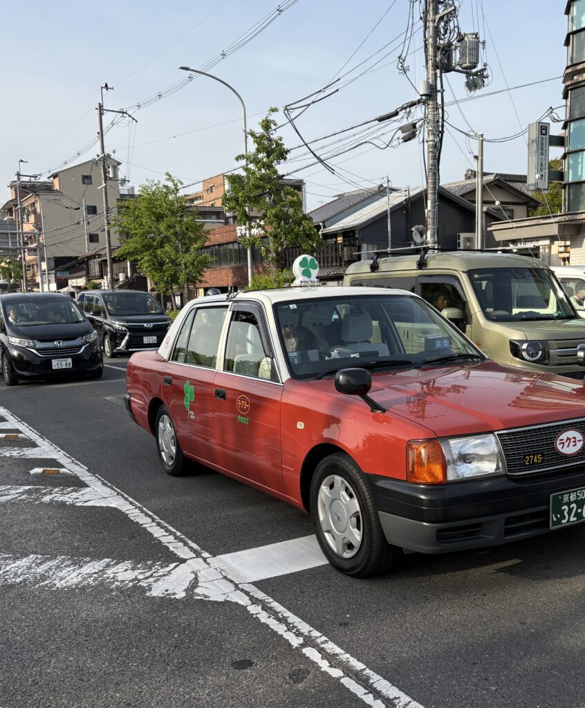 Classic red Kyoto taxi driving down a city street, showcasing local transportation in Japan.