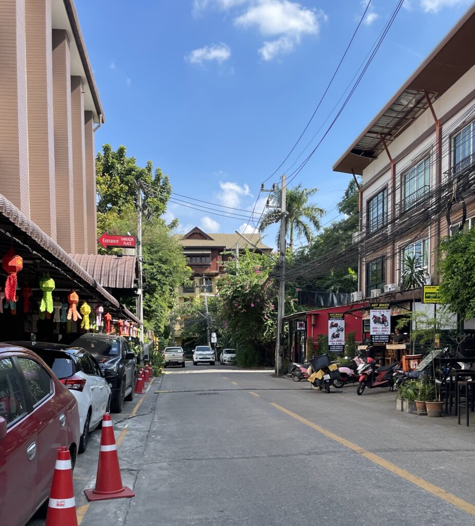 A peaceful street in Santitham, Chiang Mai, lined with local shops and restaurants, with motorbikes parked along the side.

