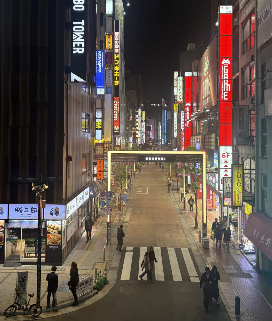 Locals walking through a lively street in Shinjuku, surrounded by colorful illuminated signs

