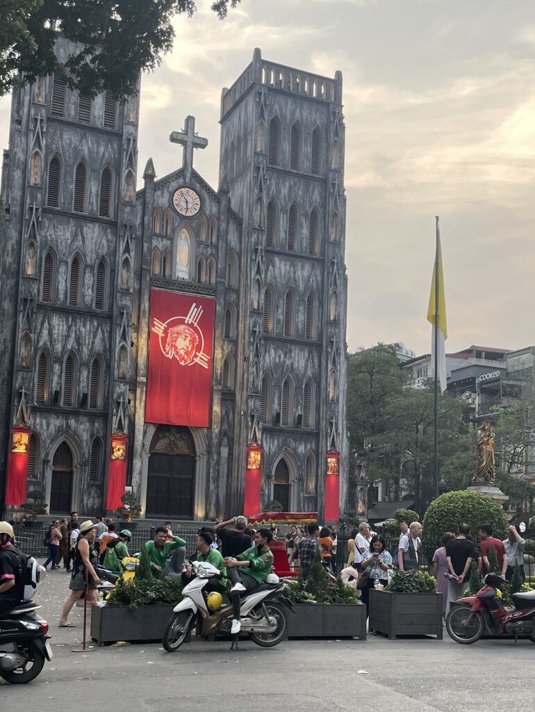 St. Joseph Cathedral in Hanoi with scooters parked out front and crowds of locals and tourists walking by