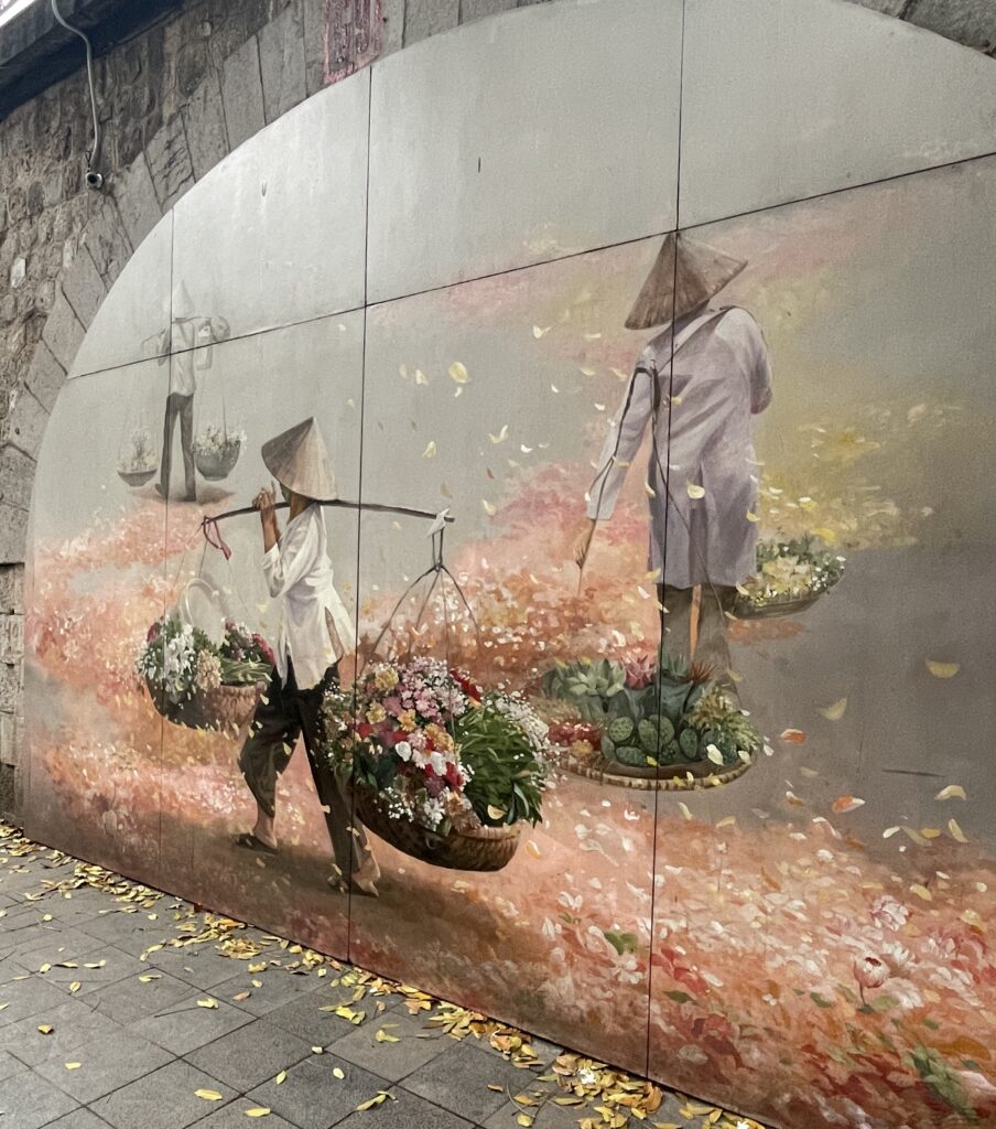 Colorful street art mural near Tay Ho (West Lake) in Hanoi, depicting a woman walking surrounded by vibrant flowers.