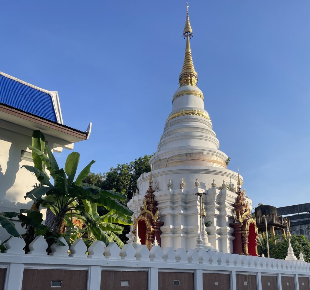 A stunning white temple with a golden tip in Chiang Mai at sunset, surrounded by historic temple walls.