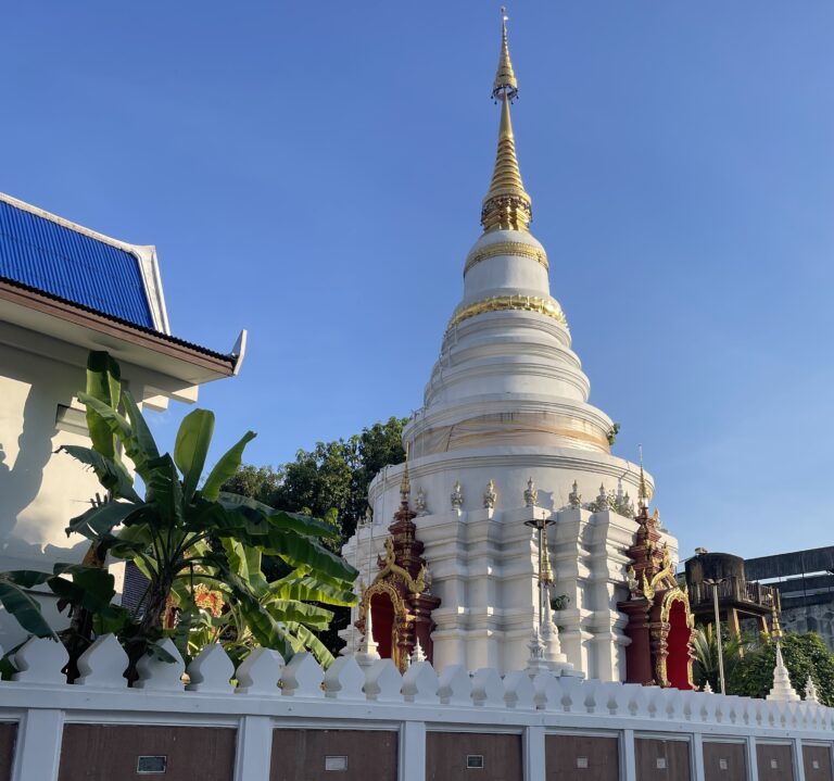 A stunning white temple with a golden tip in Chiang Mai at sunset, surrounded by historic temple walls.
