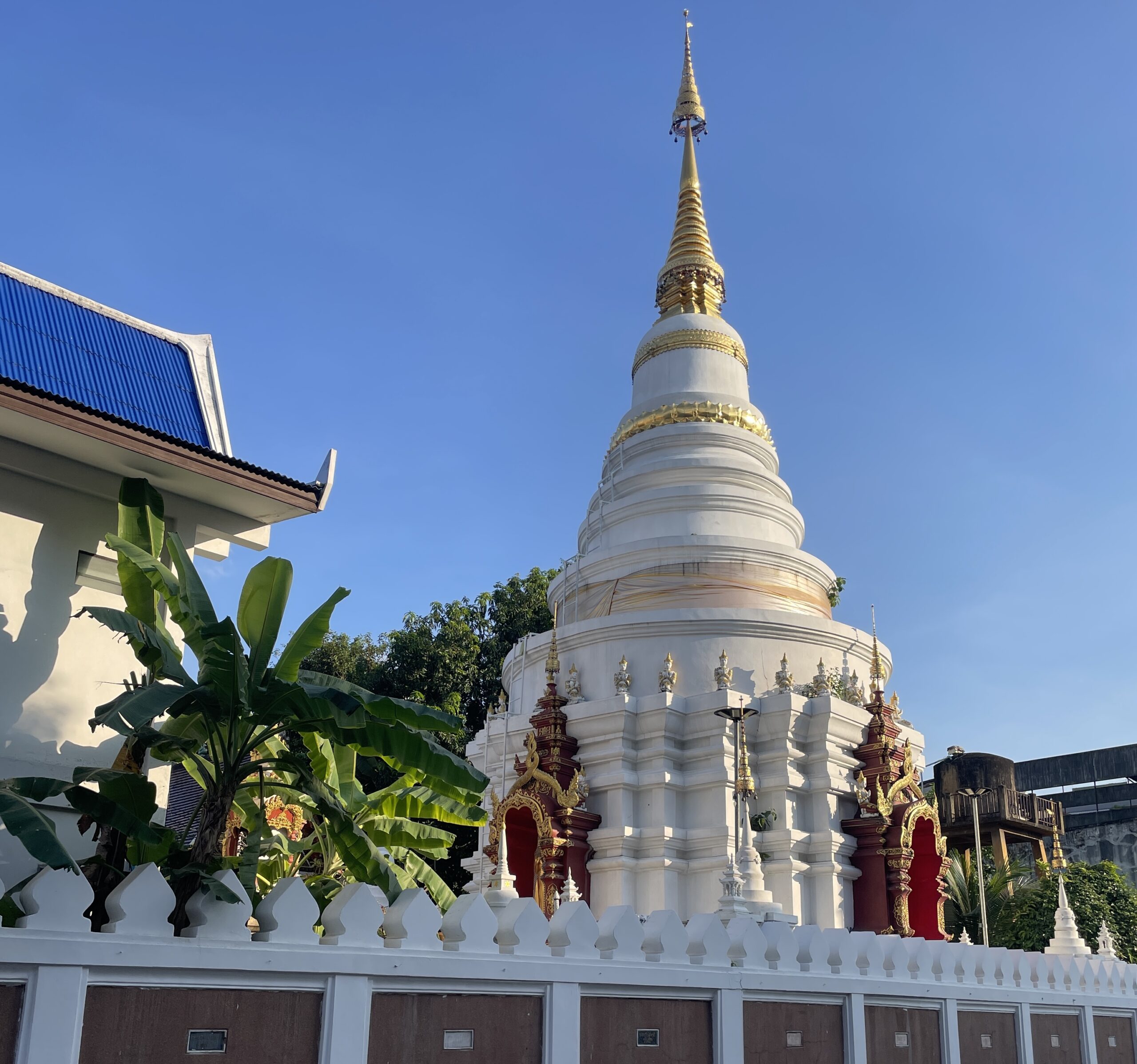 A stunning white temple with a golden tip in Chiang Mai at sunset, surrounded by historic temple walls.