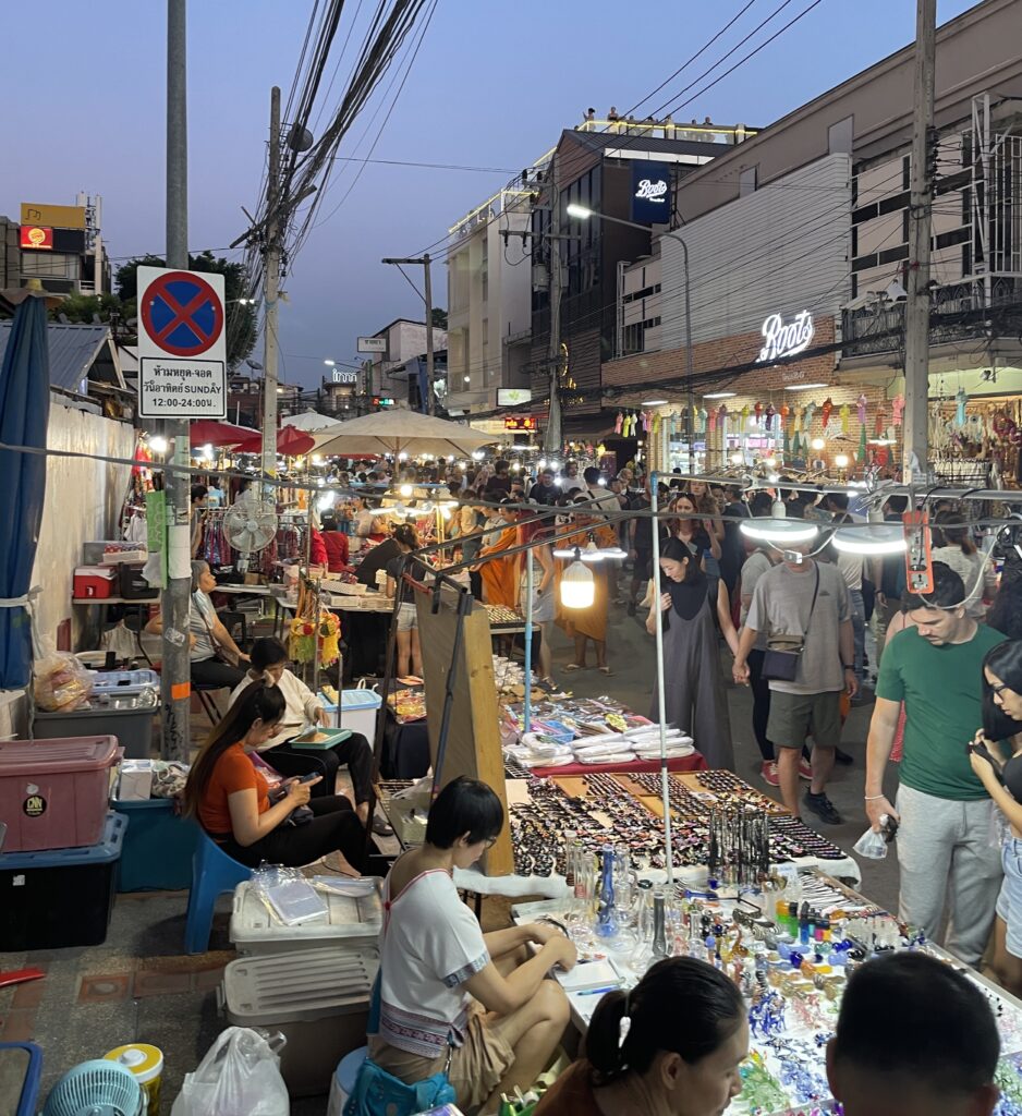 Vendors and locals at Chiang Mai’s Sunday Night Market in the Old City during the evening, with tourists browsing items at various stalls.