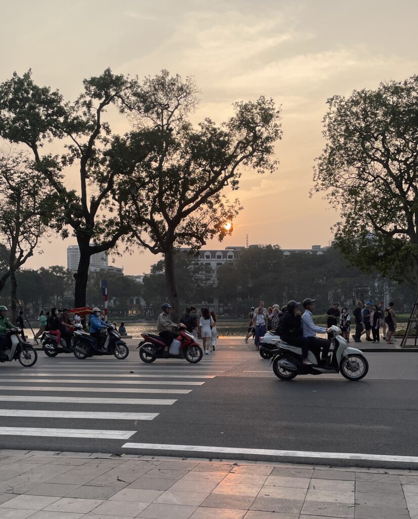 Sunset hour near Hoan Kiem Lake in Hanoi with scooters passing by