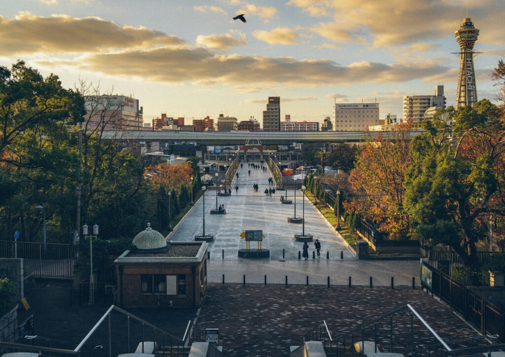 Peaceful autumn evening in Tennoji Park with colorful foliage and the Hitachi Building visible in the background skyline.
