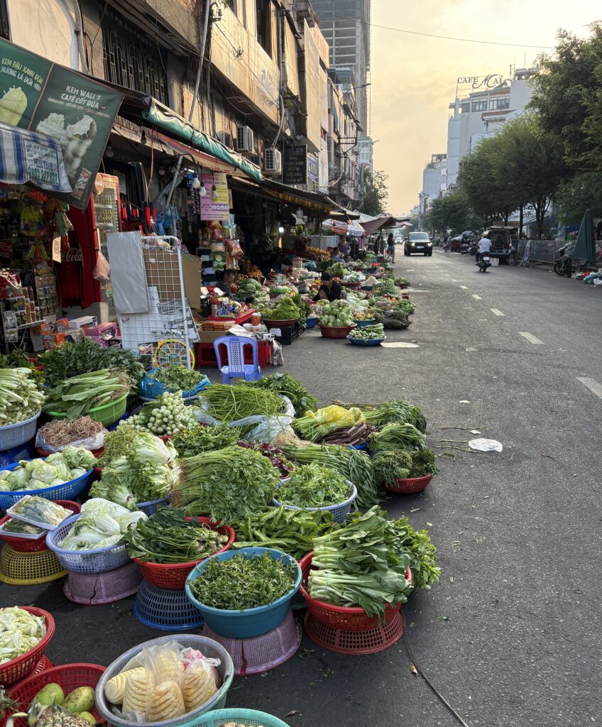 Colorful assortment of fresh vegetables displayed at a lively street market in Ho Chi Minh City, with local vendors and bustling shoppers