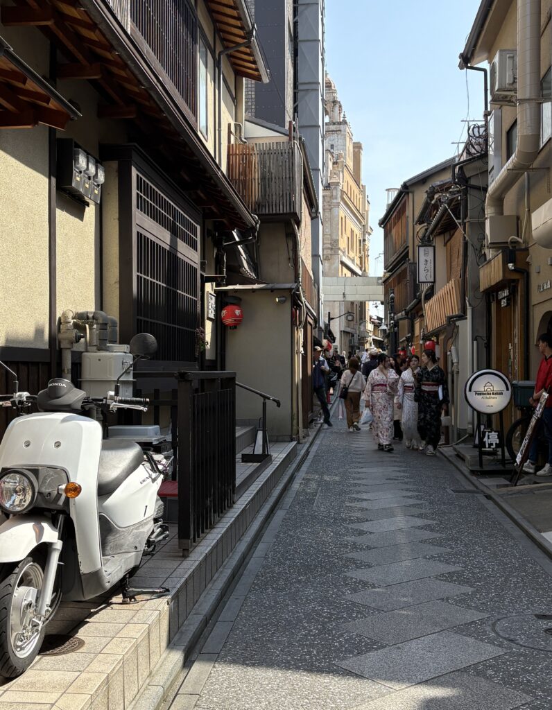 Woman in traditional kimono walking down a quiet side street in Kyoto, surrounded by historic wooden buildings and lanterns