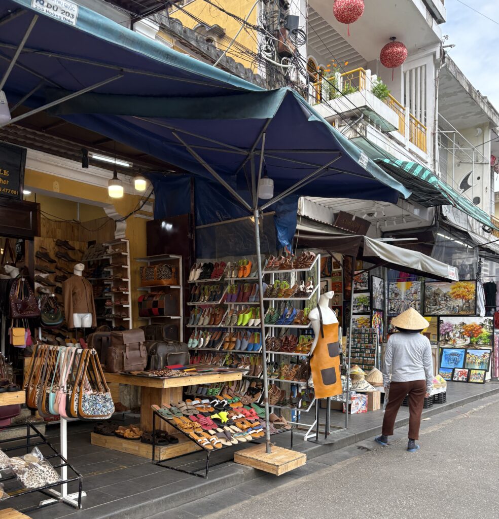 Woman in traditional conical hat selling slippers and bags outside her Hoi An shop