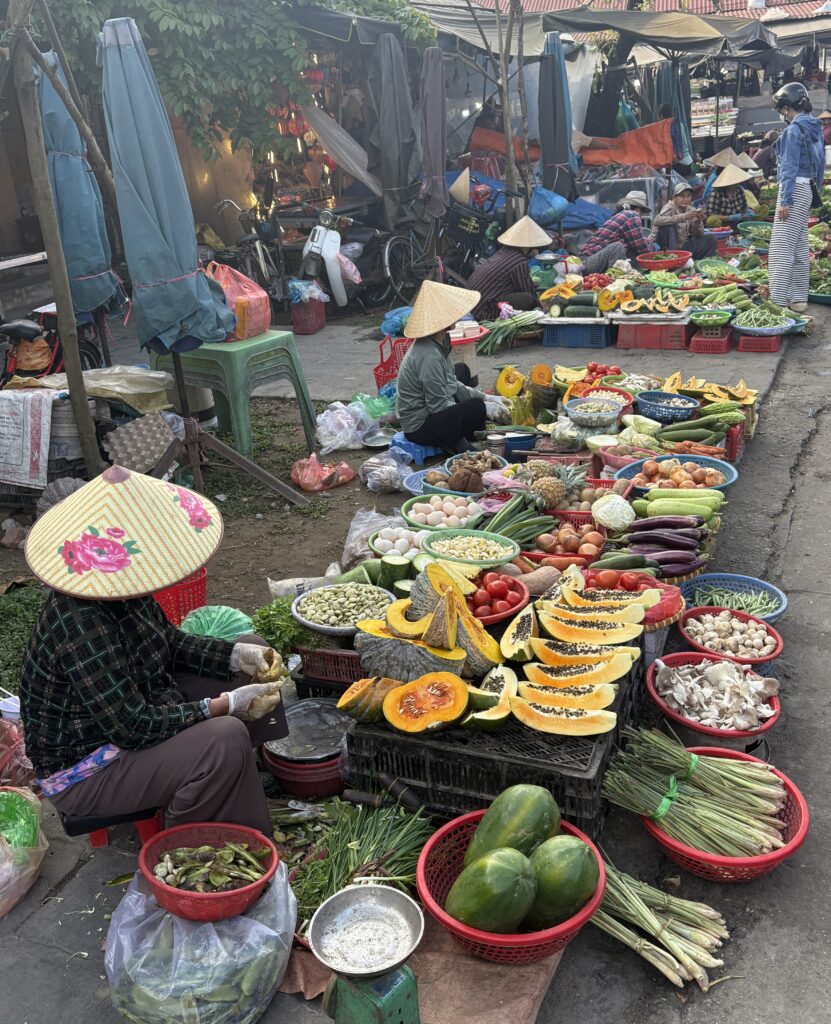 Local women wearing traditional Vietnamese hats selling colorful fruits at Hoi An’s bustling morning market
