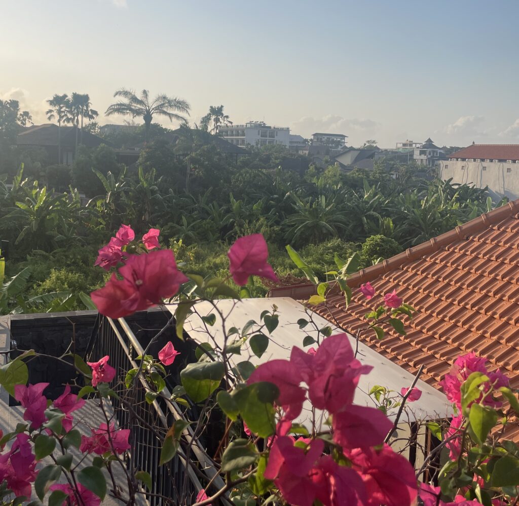 Beautiful flowers on a sunny morning with a Balinese rooftop, hotel structure, and lush greenery showcasing Bali’s natural beauty
