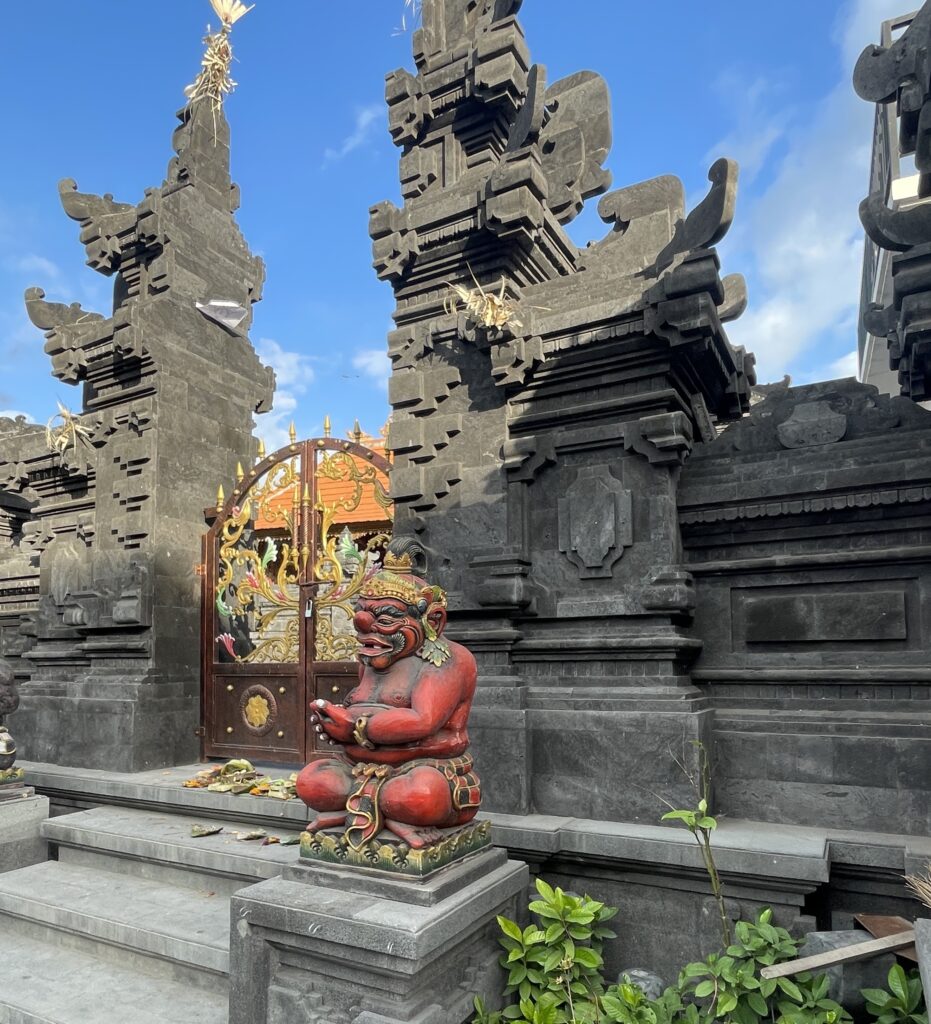 Traditional Balinese temple with a bright red statue at the entrance on a sunny day