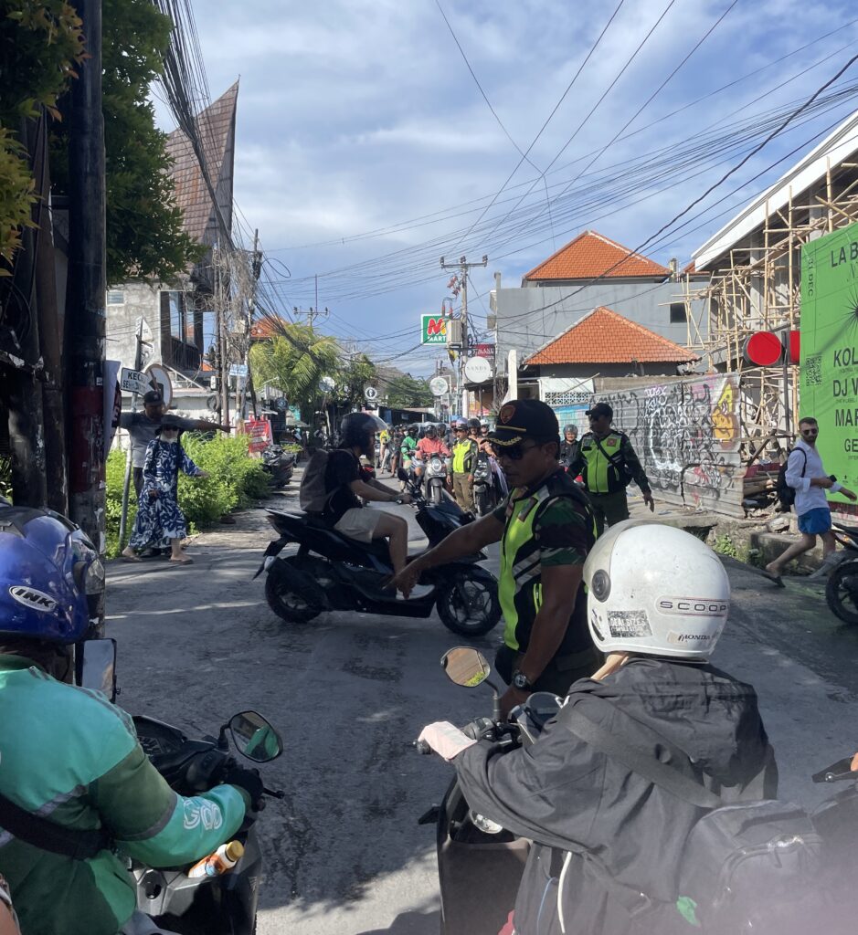 Busy traffic intersection in Canggu, Bali with a local police officer directing scooters on a tight, crowded road