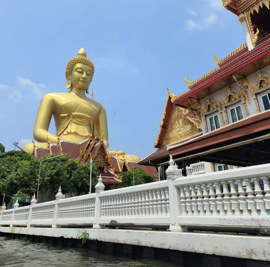 Longtail canal boat passing Wat Intharawihan's giant standing golden Buddha in Bangkok on a clear sunny day