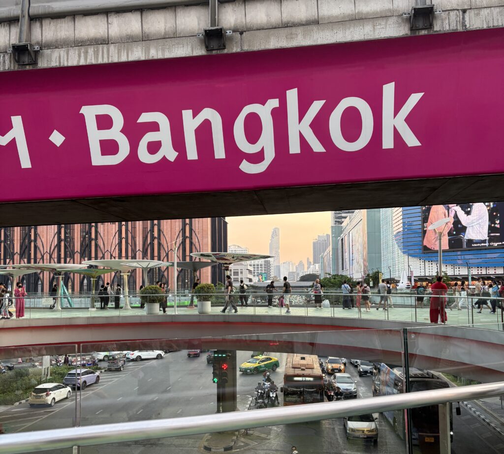 Classic Bangkok sign with evening traffic below and elevated walkway near MBK Center in Thailand