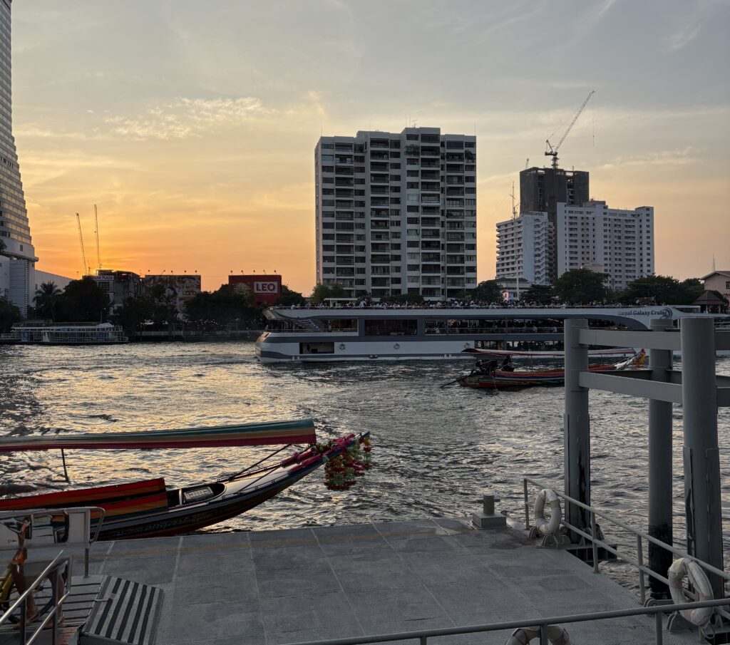 Sunset view on the Chao Phraya River in Bangkok with a large river cruise passing and a docked canal boat nearby