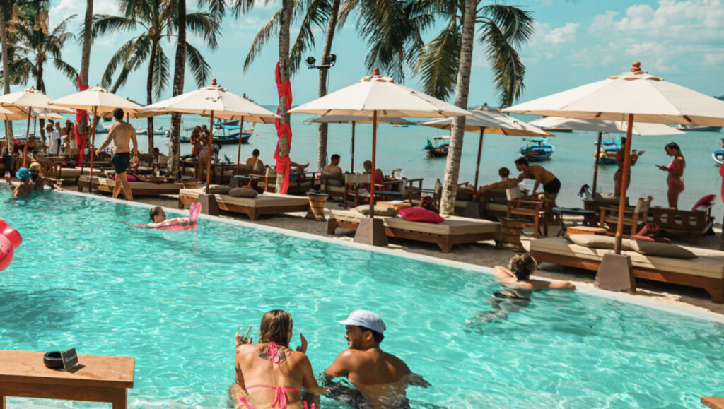 Visitors enjoying the pool with plenty of sunbeds by the beach at Carpe Diem Beach Club in Phuket.