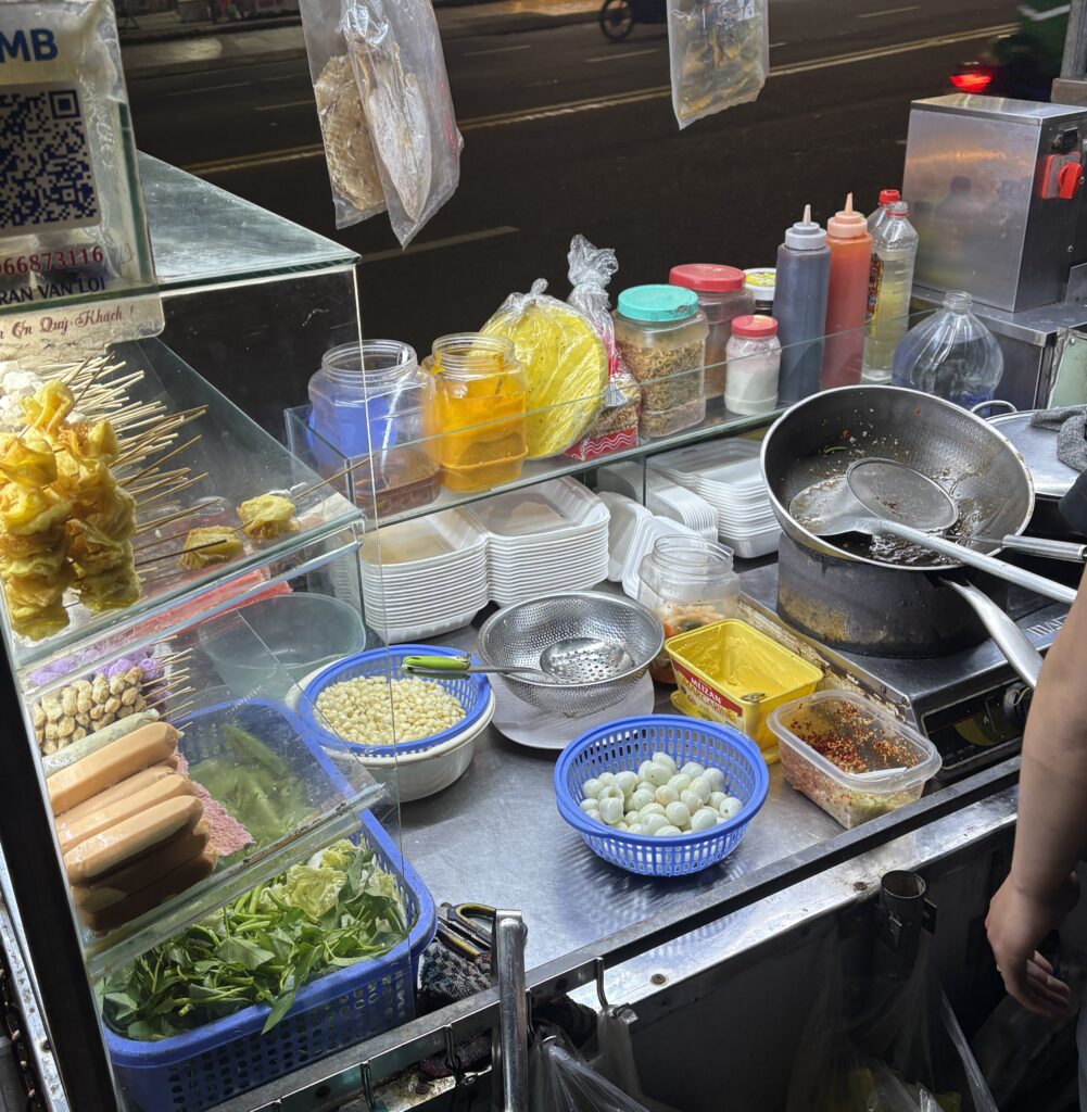 A street vendor in Da Nang at night with a brightly lit stall full of fresh ingredients
