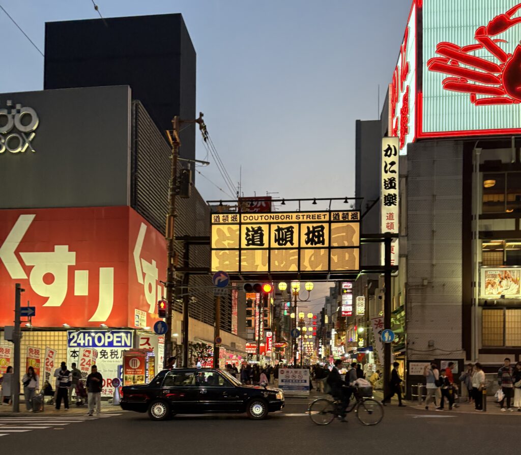 Brightly lit Dotonbori sign in Osaka at night with a car and bicycle passing by