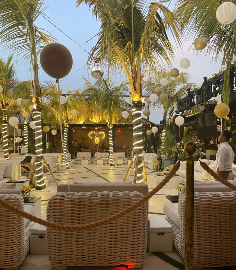 Luxury beach club El Kabron in Bali during evening hour with elegant decor, palm trees, rope sectioning, and upscale ambiance