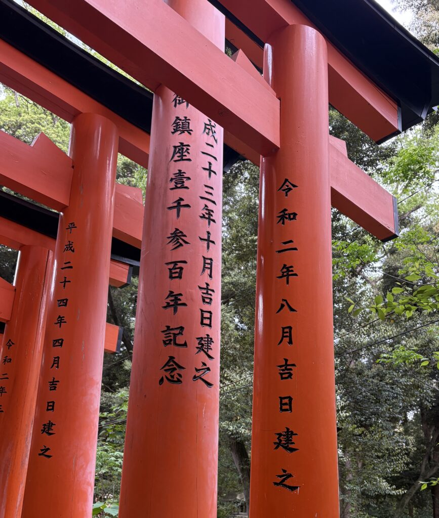 Close-up of the red torii pillars at Fushimi Inari Taisha shrine in Kyoto, Japan with black Japanese lettering and forest background.