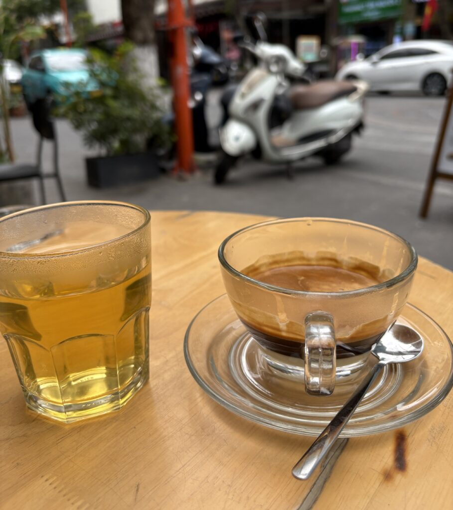 Hot Vietnamese condensed milk coffee served with a glass of tra da iced tea in Da Nang, with a scooter in the background