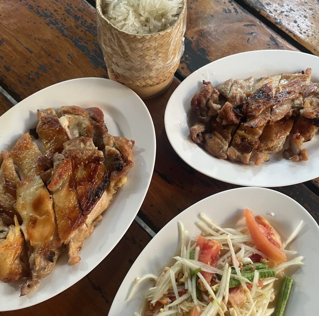 Thai grilled chicken (Kai Yang) served with papaya salad and sticky rice on two plates in Chiang Mai, Thailand.