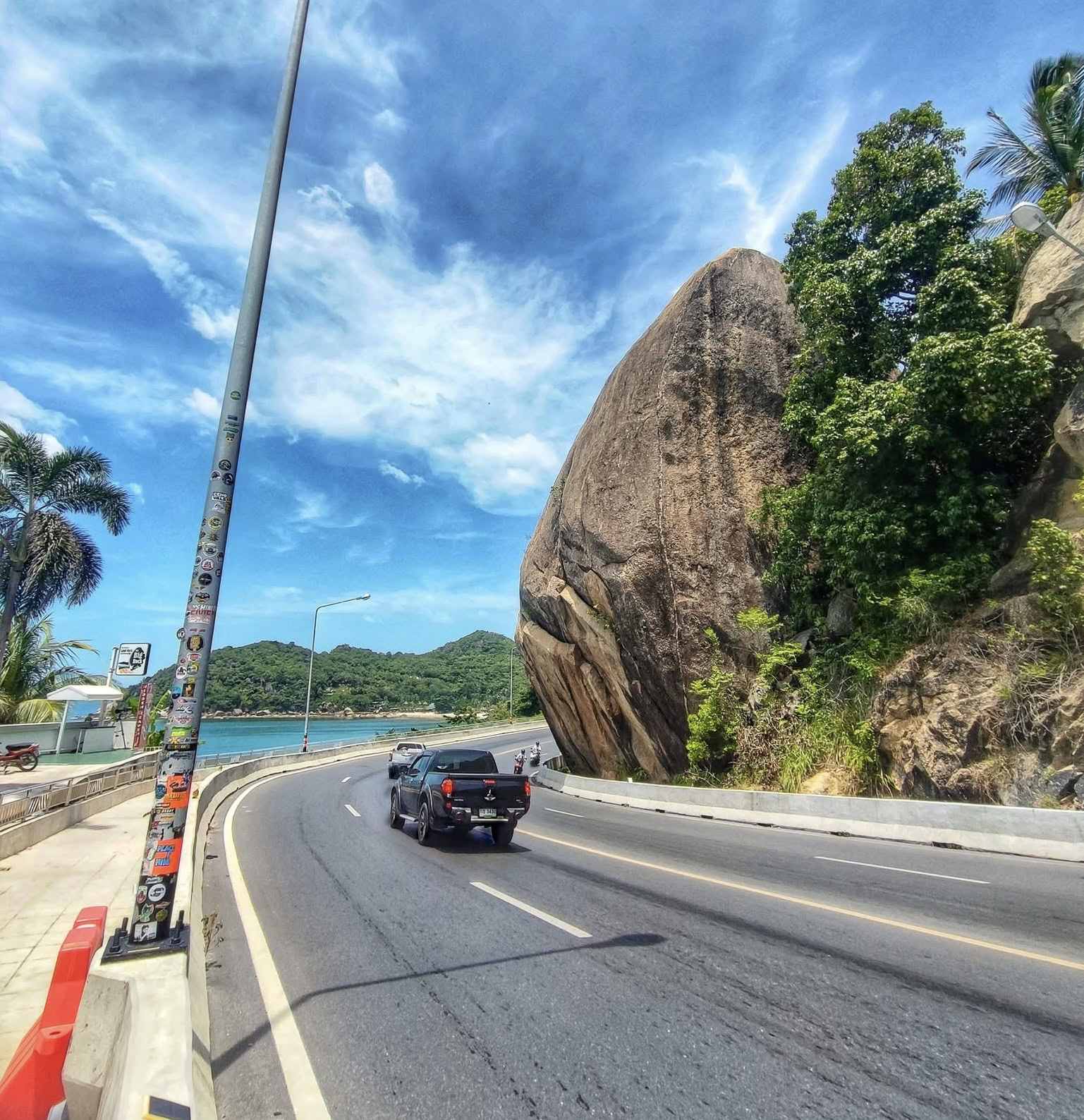Scenic coastal road in Koh Samui with the sea on the left and a large rock on the right on a clear day