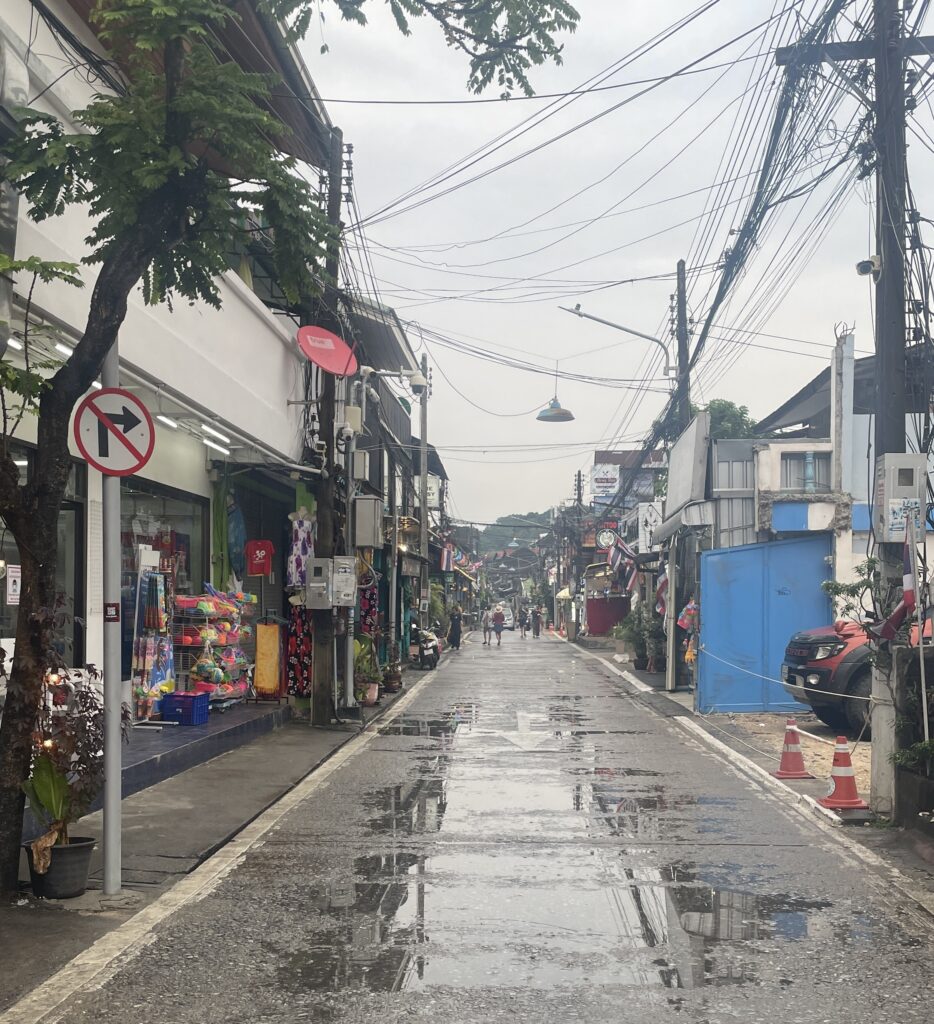 Rain puddles reflecting buildings on a street in Koh Samui during Thailand’s monsoon season.