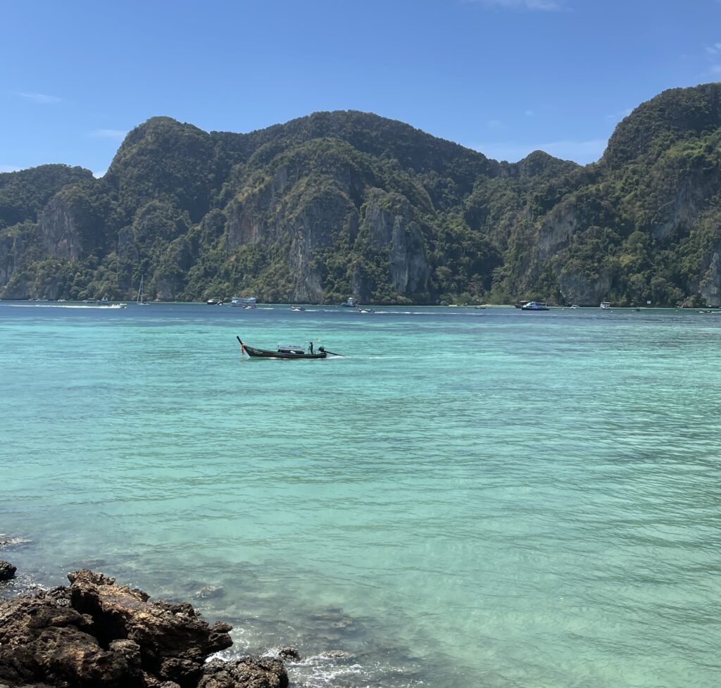 A longtail boat on the crystal clear blue waters of Phi Phi Island with towering limestone cliffs in the background.