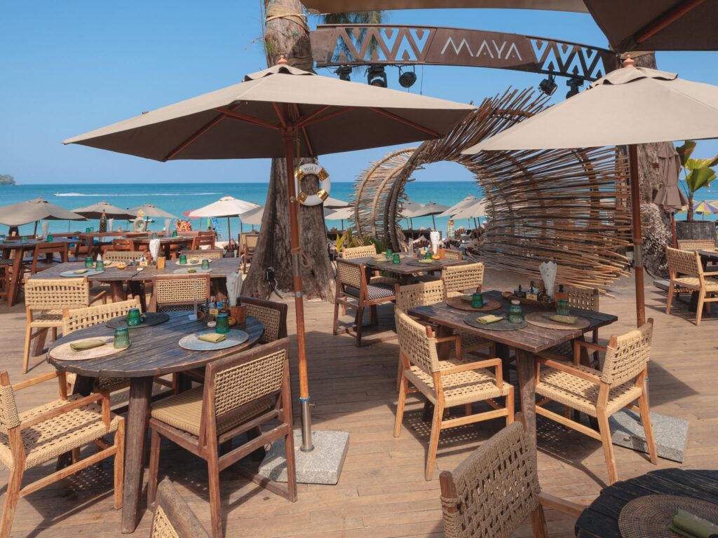 Rustic dining chairs and beachside sunbeds at Maya Beach Club in Phuket, offering a relaxed tropical vibe.