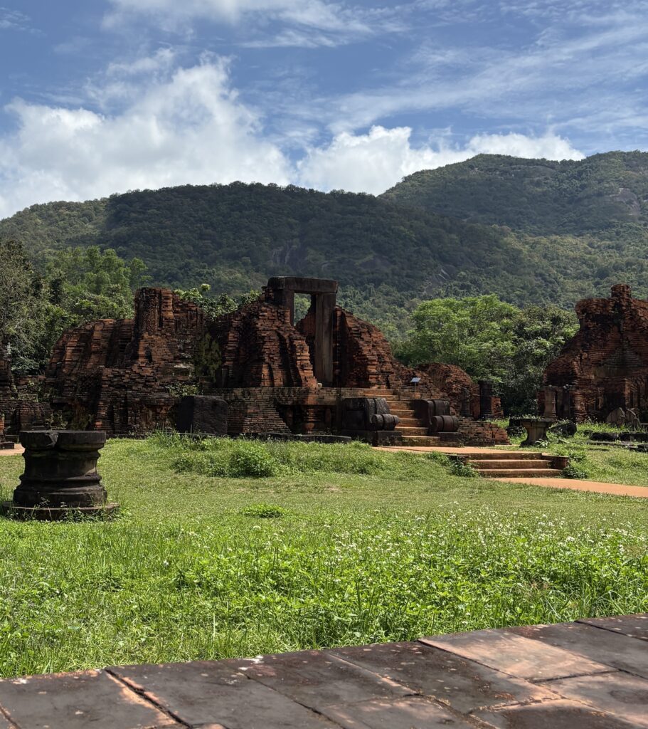 Landscape view of My Son Sanctuary with mountains in the background on a sunny day.
