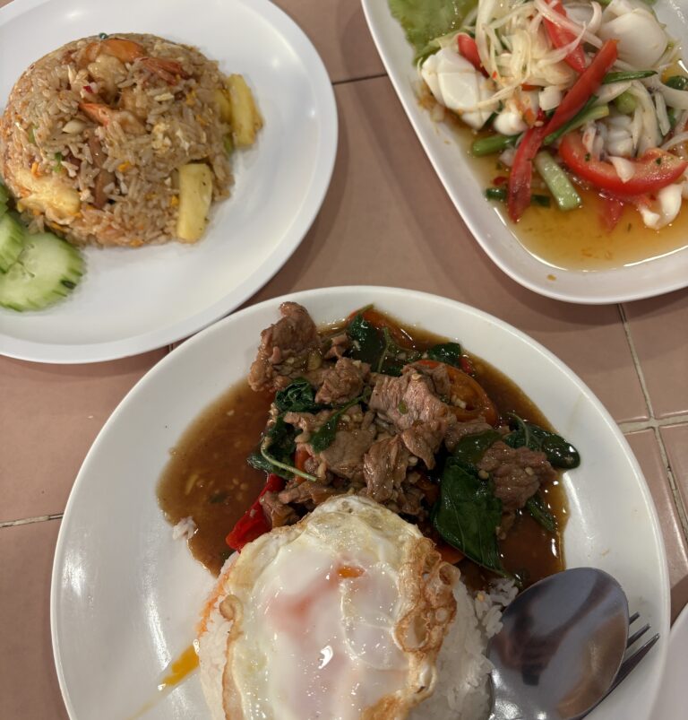 A table spread featuring Pad Kra Pao, Thai squid salad, and Tom Yum fried rice, showcasing vibrant Thai flavors.