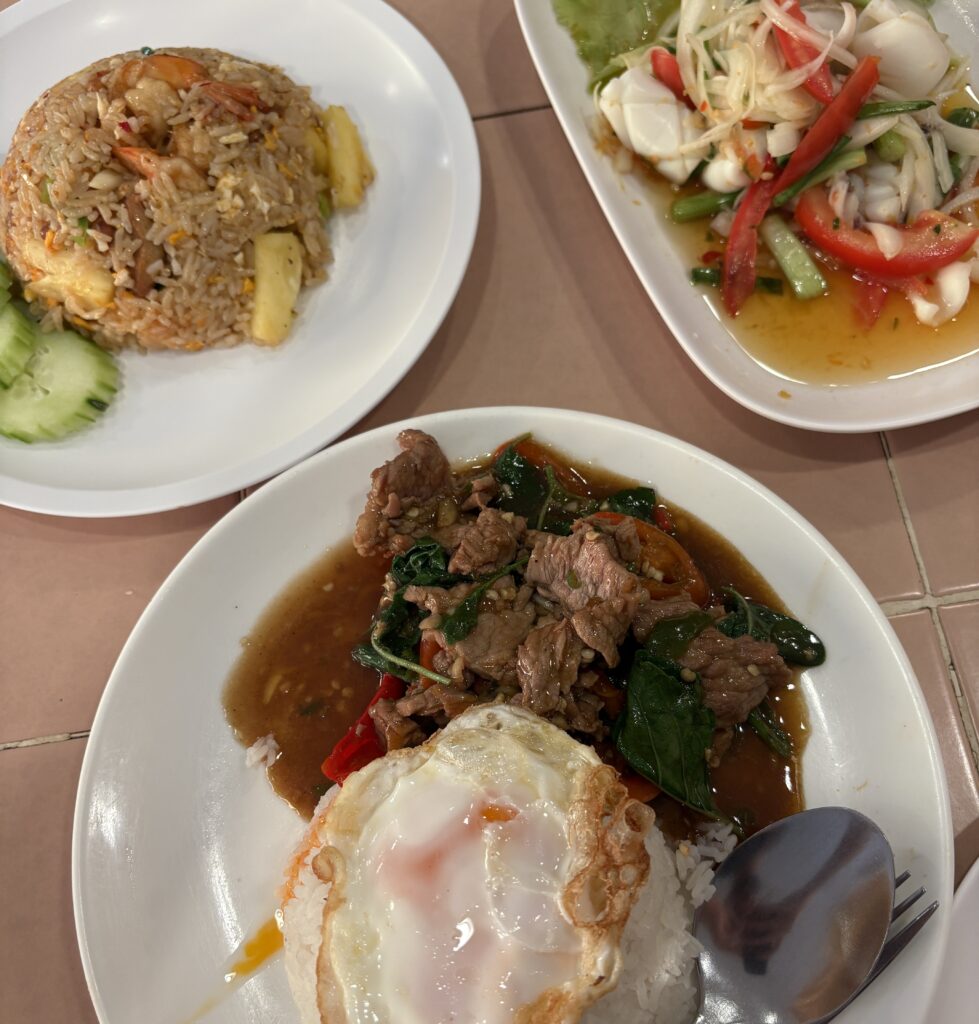A table spread featuring Pad Kra Pao, Thai squid salad, and Tom Yum fried rice, showcasing vibrant Thai flavors.