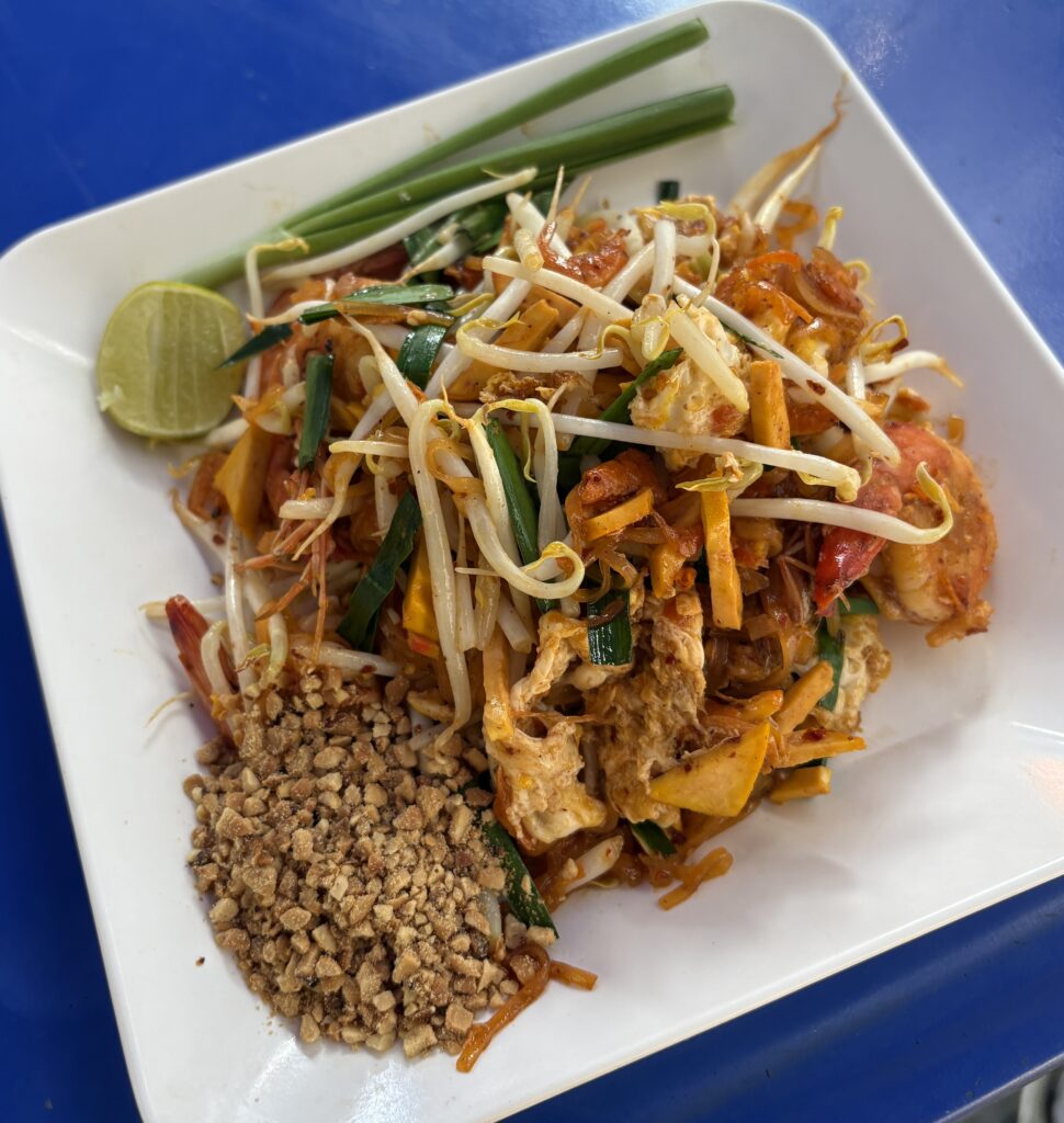 Freshly served Pad Thai with vibrant colors, topped with bean sprouts, lime, and a pile of crushed peanuts on the plate.
