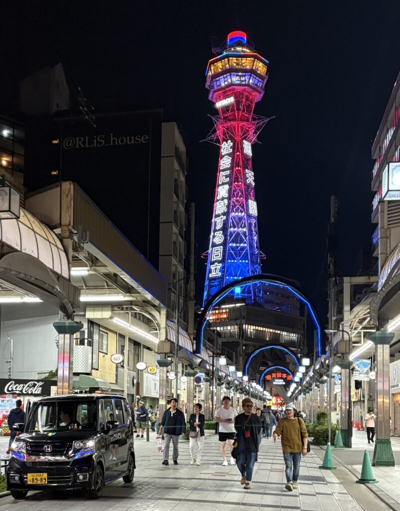 Laid-back Shinsekai street in Osaka at night with Tsutenkaku Tower lit up in the background