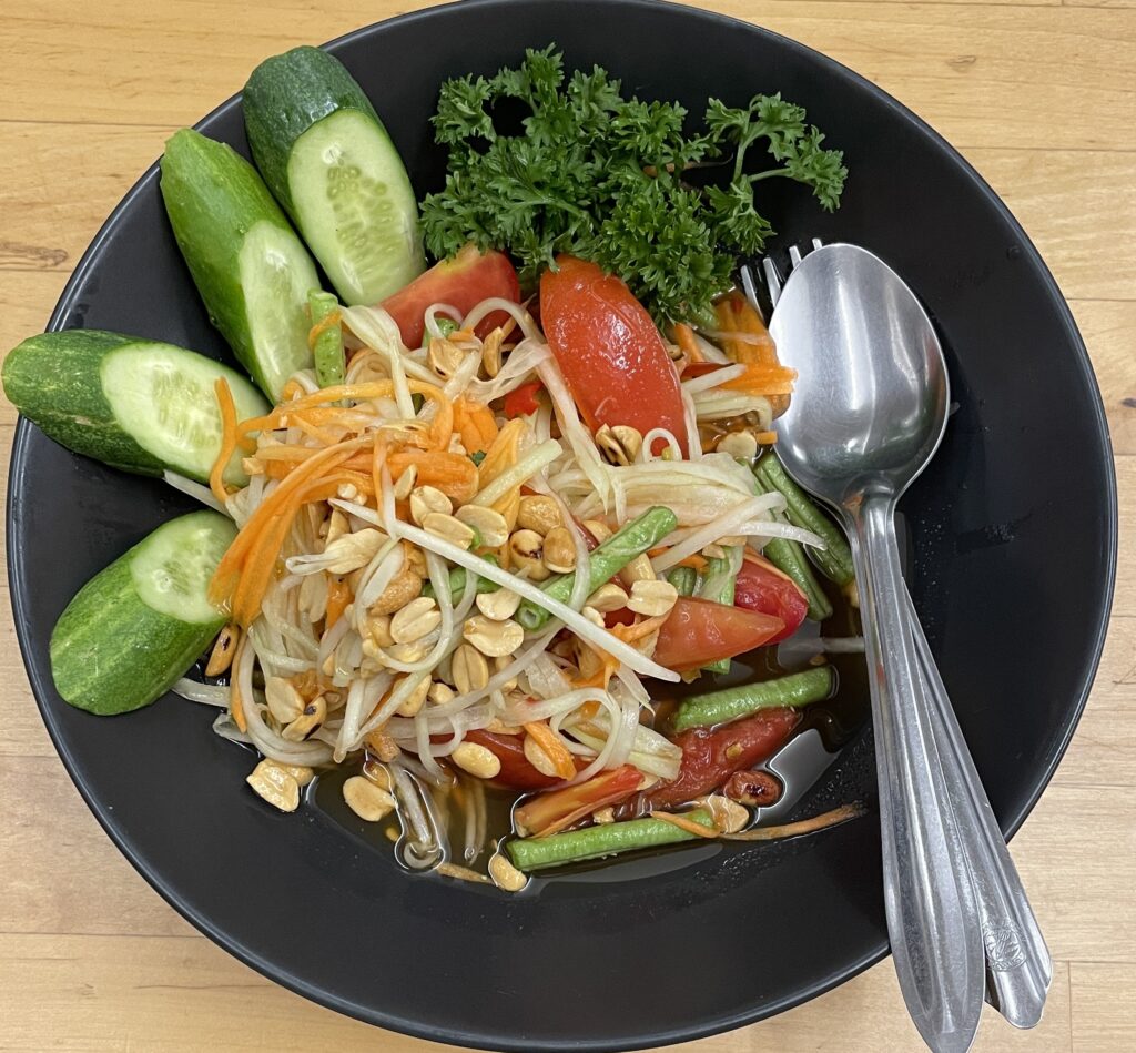 Close‑up of Som Tum papaya salad with shredded green papaya, peanuts, tomatoes, and chili on a plate.