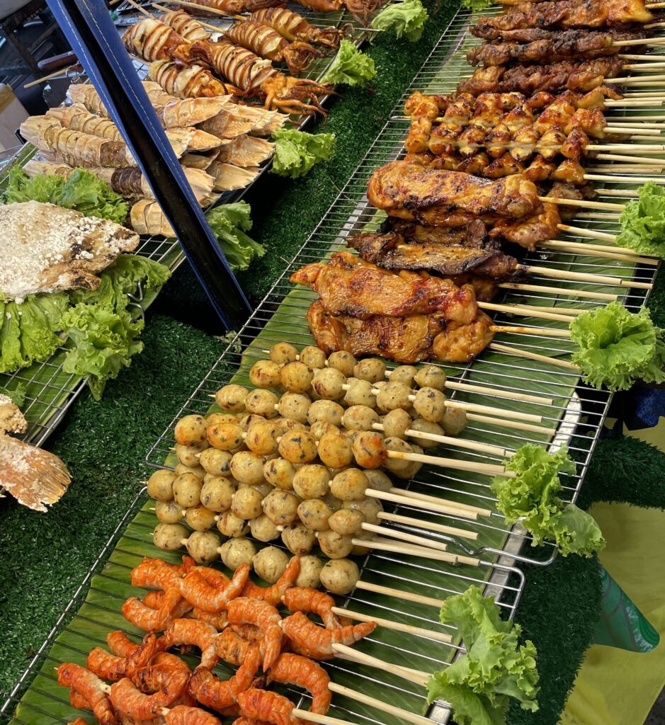 A street food stall in Thailand displaying a variety of grilled skewers, including chicken, prawns, and shrimp, ready for hungry visitors.